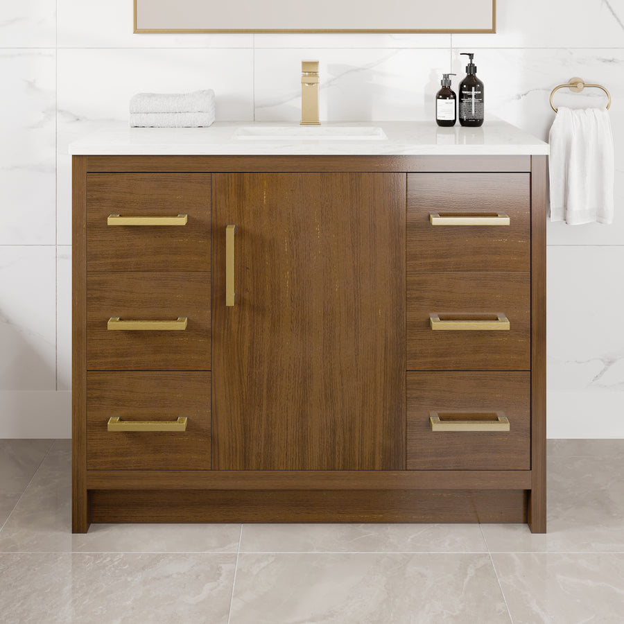 The Curio 42″ Vanity in Walnut features a modern wood finish, gold handles on six drawers, and a white Carrara quartz countertop with an integrated sink. The vanity is styled with two soap dispensers, a folded towel, and a gold towel ring holding a white towel on the right side.