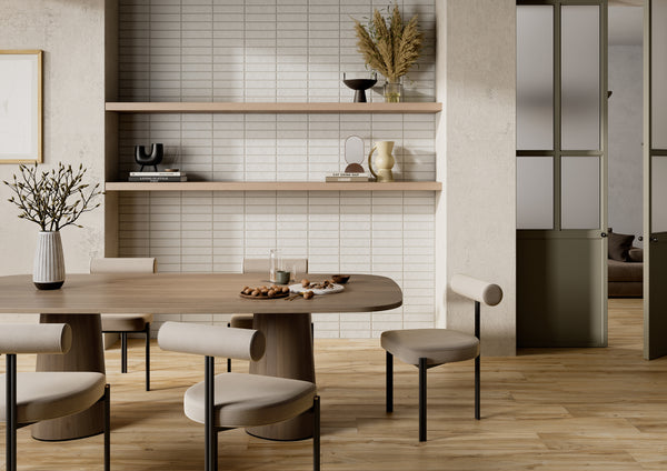 A modern dining area with a wooden table, four cushioned chairs, and minimalist decor. Shelves with vases and dried plants are mounted on a tiled wall. Light wood flooring and neutral tones create a calm atmosphere.