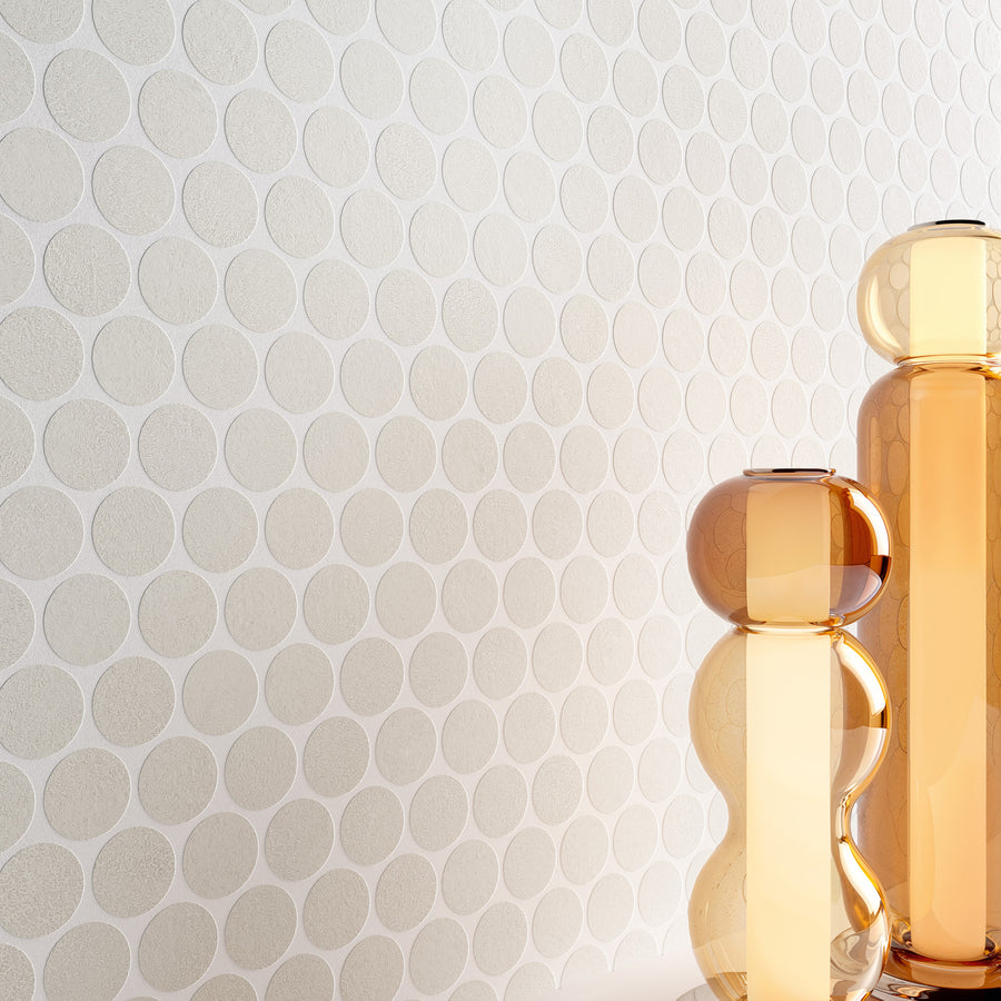 Two tall, amber-colored glass vases with rounded shapes stand in front of a light wall covered in a subtle circular pattern. The scene is minimalistic and modern.