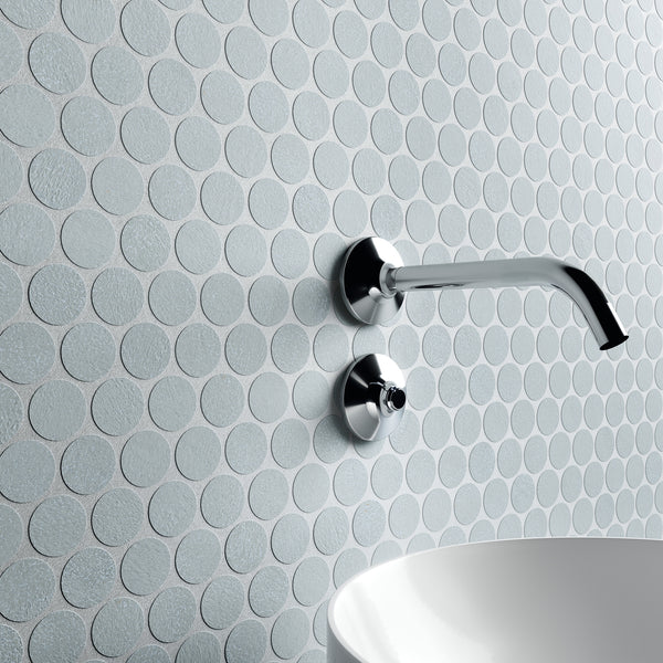 A modern bathroom wall with round, textured, light gray tiles, featuring a minimalist chrome faucet and handle above a white, curved basin sink.