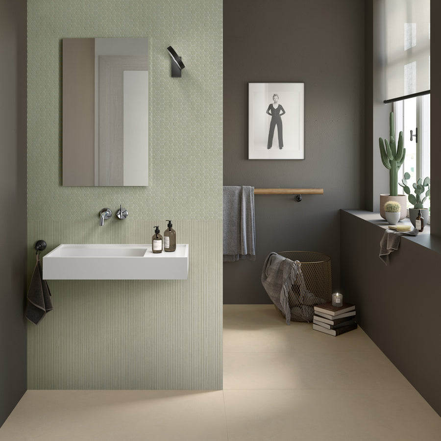 Modern bathroom with light green and grey walls, a rectangular mirror above a white floating sink, black fixtures, a towel rail, potted plants, books, a candle, and a framed black-and-white photo on the wall.