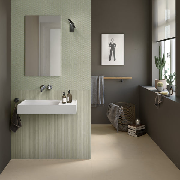Modern bathroom with light green and grey walls, a rectangular mirror above a white floating sink, black fixtures, a towel rail, potted plants, books, a candle, and a framed black-and-white photo on the wall.