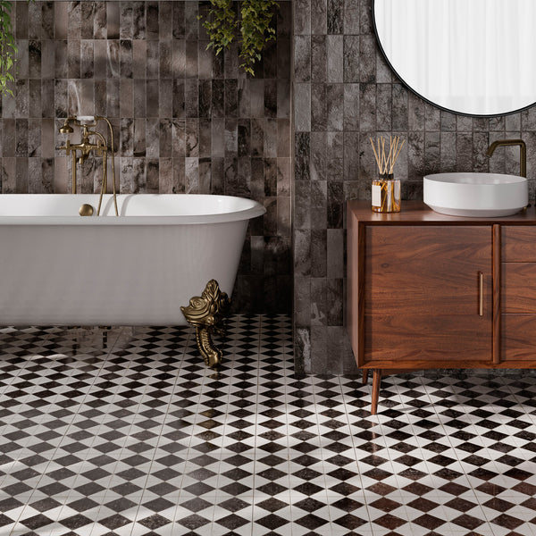 A bathroom with a freestanding white bathtub on ornate gold feet, dark patterned wall tiles, black and white checkered floor, a round mirror, and a wooden vanity with a vessel sink.