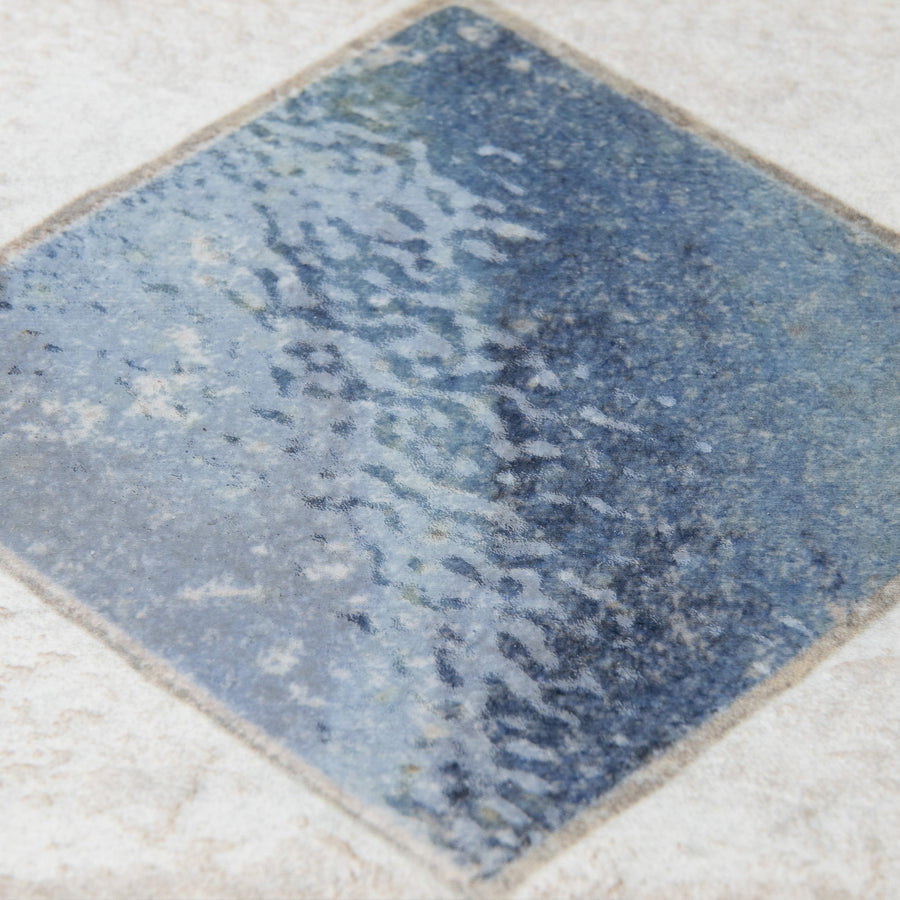 A close-up of a blue and gray textured tile with a wavy, water-like pattern, set diagonally on a light beige tiled surface.