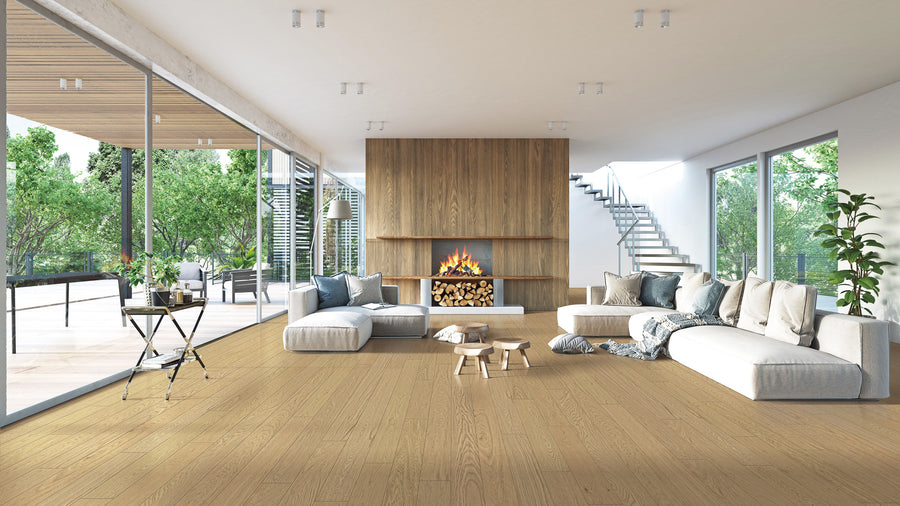 Modern living room with large windows, light wood floors, corner sofas, a central coffee table, indoor plants, and a wood-paneled fireplace with stacked logs. Bright, open space with outdoor views and a staircase visible.