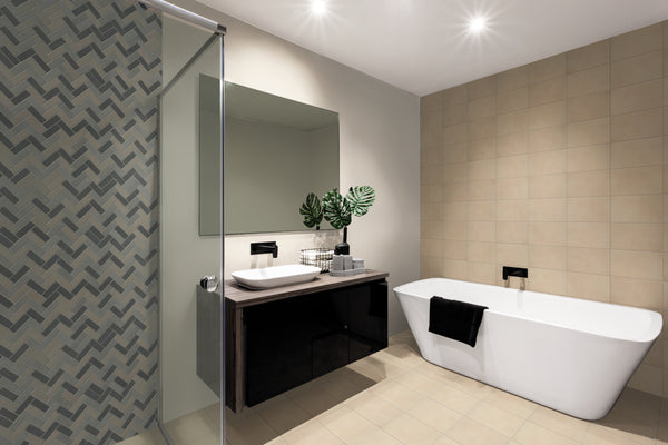 Modern bathroom with beige tiled walls, a luxury mosaic accent wall, white freestanding tub, glass shower featuring Ardennes Herringbone Mosaic Tile in Blend, large mirror, and dark vanity with vessel sink and green leafy plants.