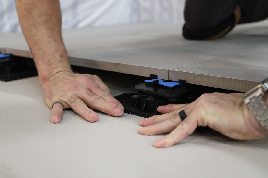 A hand examines components of the Ardex TerraMaxx Pedestal system on a table—ideal for installing raised flooring with porcelain tiles on roof terraces.