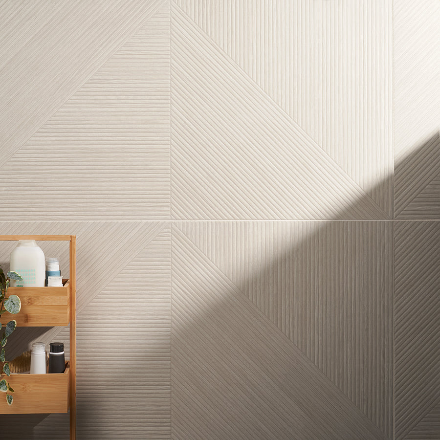 A wooden shelf with toiletries and a trailing plant stands against a geometric beige wall with textured, diagonal lines. Sunlight casts a soft shadow across the wall.