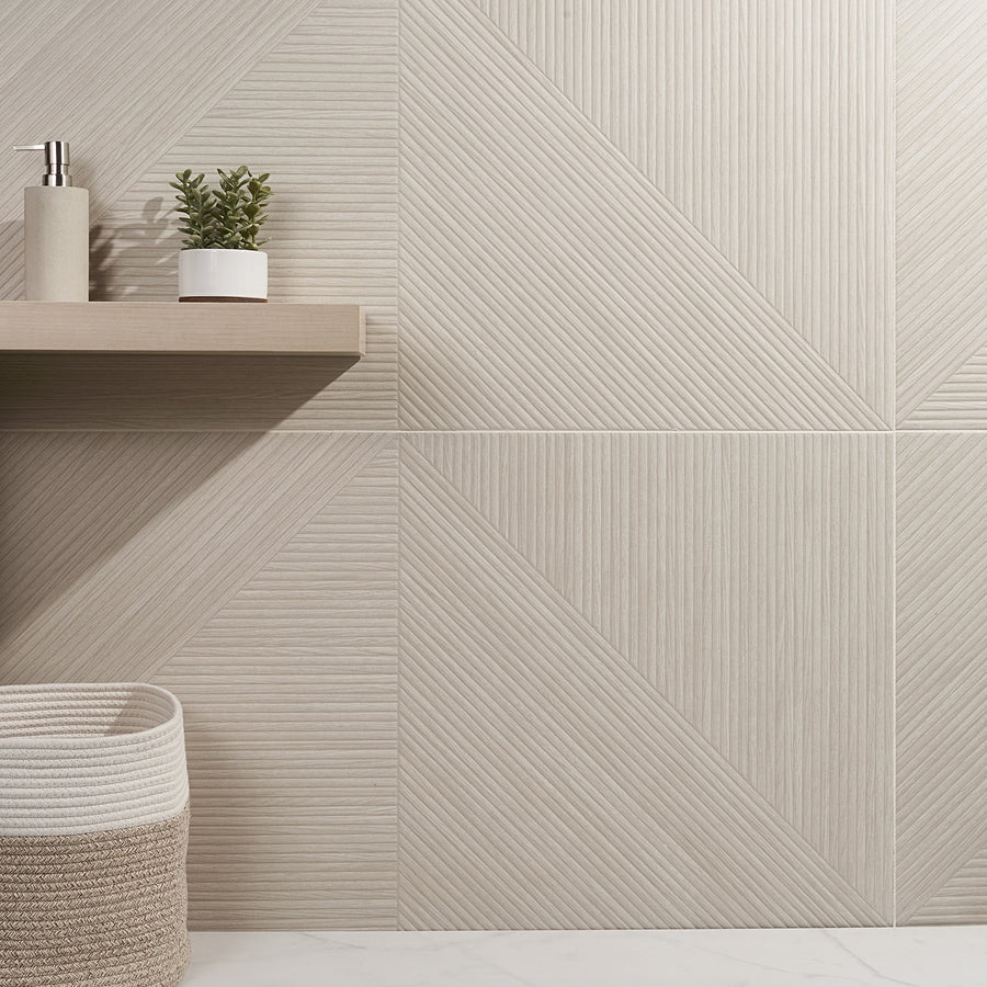 A modern bathroom with beige textured geometric tiles, a floating wooden shelf holding a small potted plant and soap dispenser, and a woven basket on a white marble floor.