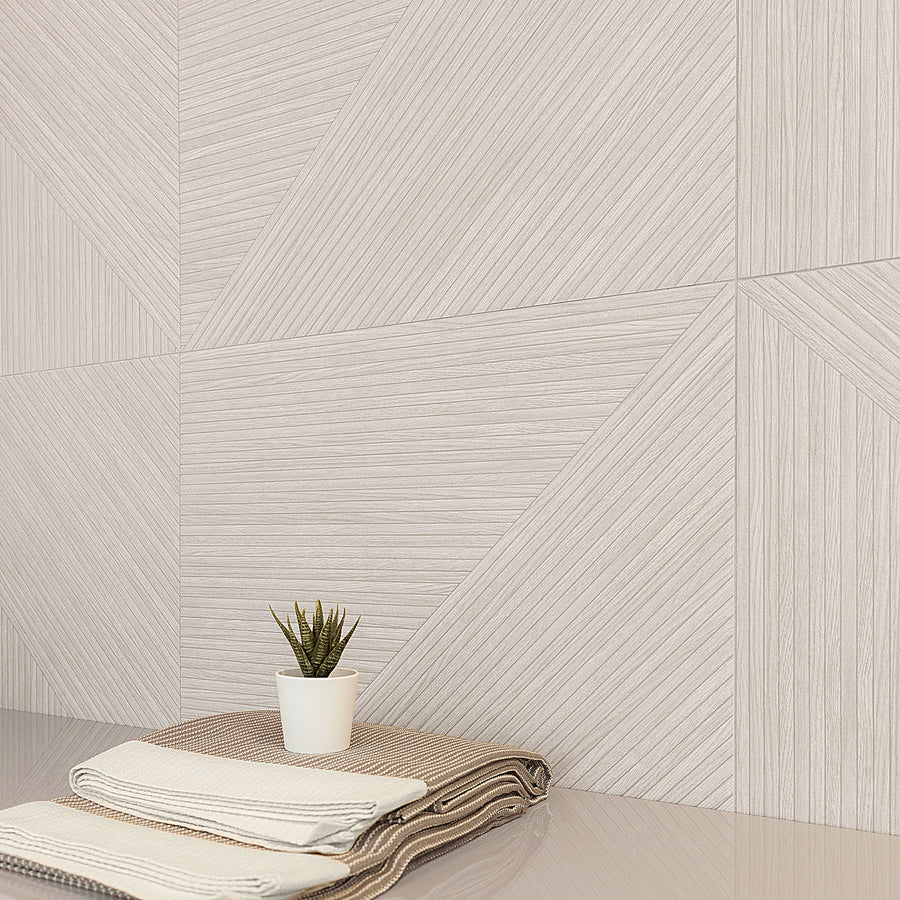 A small potted plant sits on a folded stack of patterned towels atop a glossy surface, with a modern wall in the background featuring geometric patterns of diagonal and vertical lines in neutral tones.