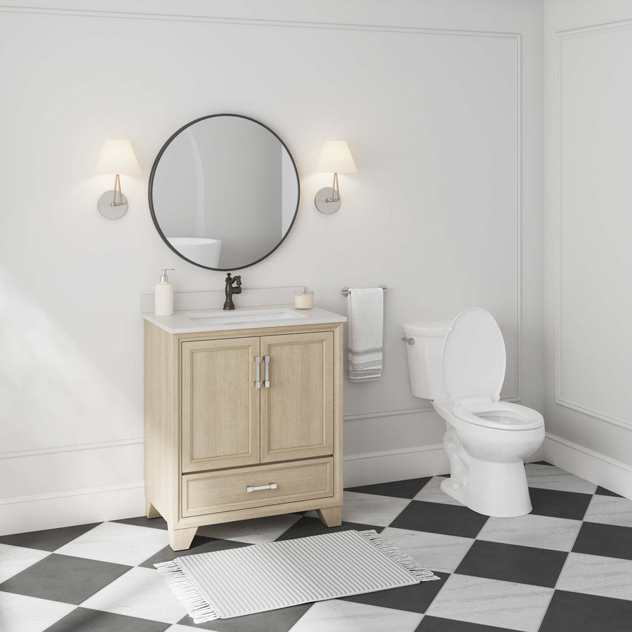 A modern bathroom with a light wood vanity, round mirror, two wall sconces, white toilet, towel ring with a towel, and a gray and white checkered floor with a striped rug. The decor is minimal and bright.