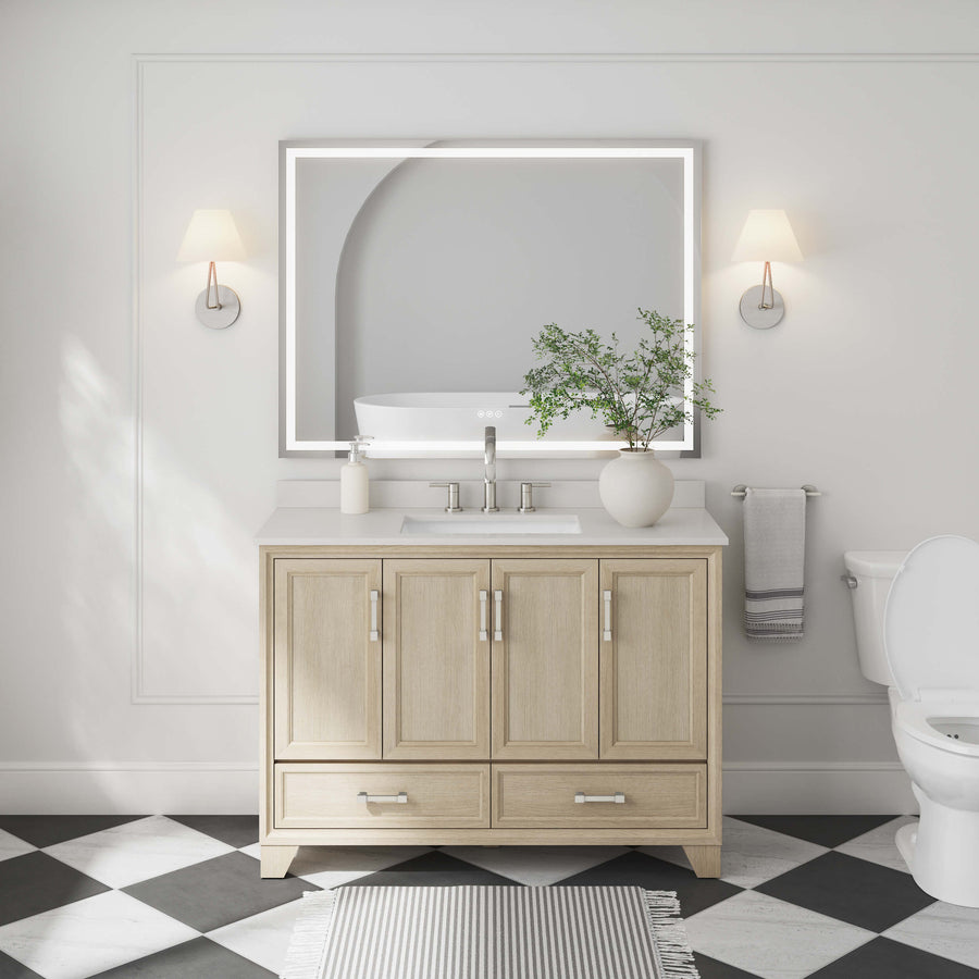 A modern bathroom showcases the Ashlow 48" Vanity with an engineered stone top, ample storage, a large illuminated mirror, wall sconces, greenery, towel, toilet, and bold black-and-white checkered floor tiles.