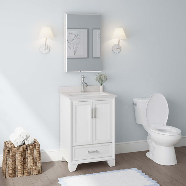 A clean, modern bathroom with a white vanity and sink, wall mirror, toilet, light blue walls, two wall lamps, framed art, a basket with towels, and a white rug on a wooden floor.