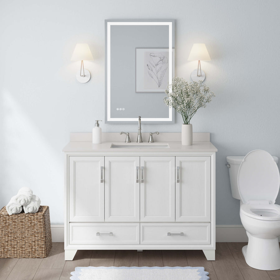 A modern bathroom features the Ashlow 48" Vanity with an engineered stone top, sink, and mirror flanked by two wall sconces. A flower vase sits on the counter, with a wicker basket of towels on the left and a toilet on the right.