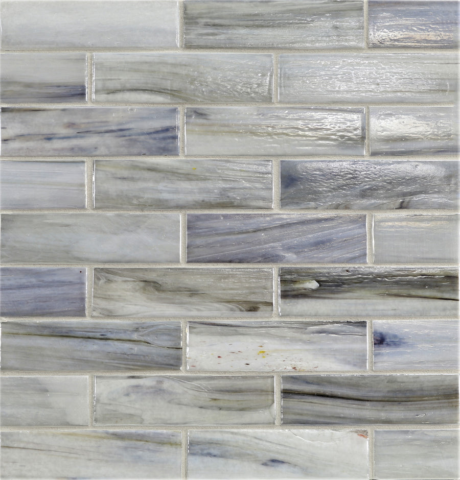 A close-up of a wall with Agate 1 1/4" x 5" Bari Mosaic Glass Tile in gray and blue tones, arranged in a staggered brick pattern with natural swirls and agate-inspired mosaic textures.