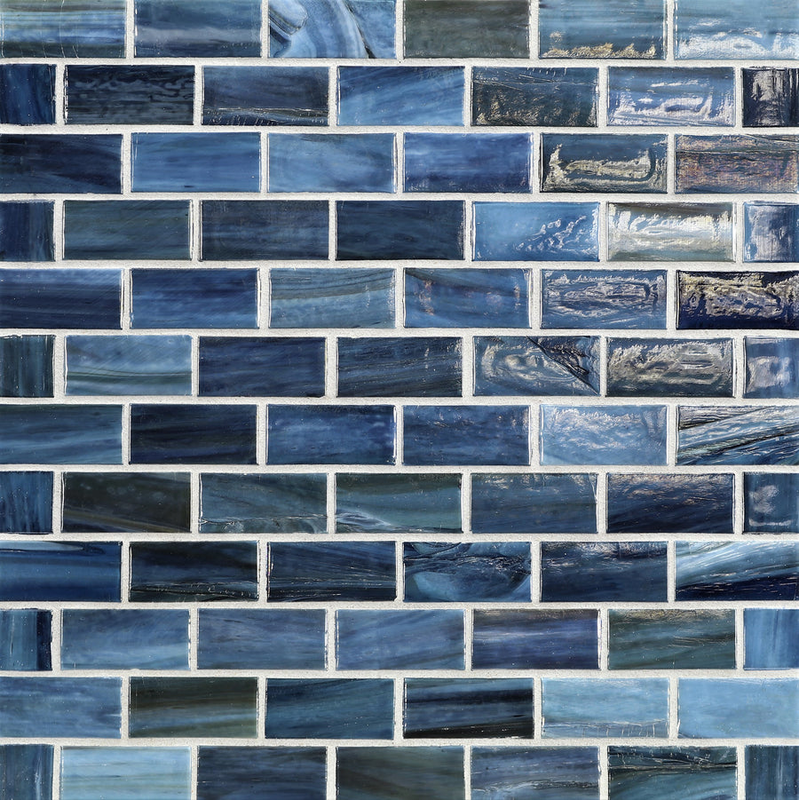 A close-up of a wall featuring Agate 1x2 Portofino Mosaic Glass Tile in rectangular blue pieces with varied shades and patterns, arranged in a brick pattern with white grout lines.