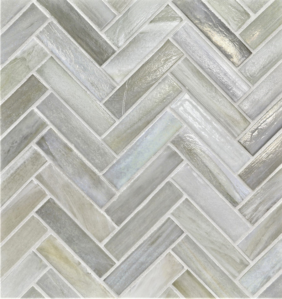 The Agate 1x4 Herringbone Asolo Mosaic Glass Tile features light grey and white pieces in a geometric pattern with subtle color variation and a glossy finish, creating a modern, textured look.