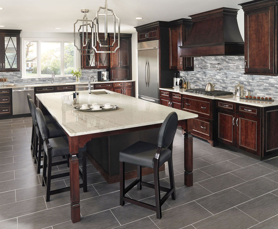 Spacious modern kitchen with dark wood cabinets, stainless steel appliances, a large island with a granite countertop, four black chairs, and gray tile flooring. The backsplash is gray and white mosaic tile.
