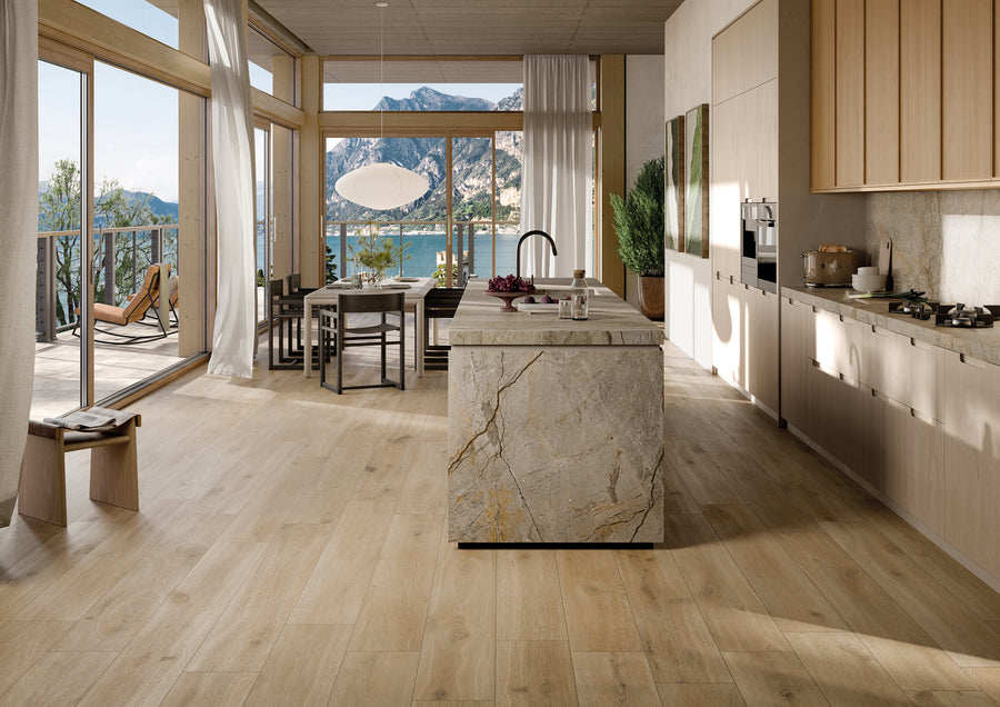 Modern kitchen and dining area with light wood floors, stone island, large windows, and mountain and lake views. Sunlight fills the space, highlighting minimalist decor and natural elements.
