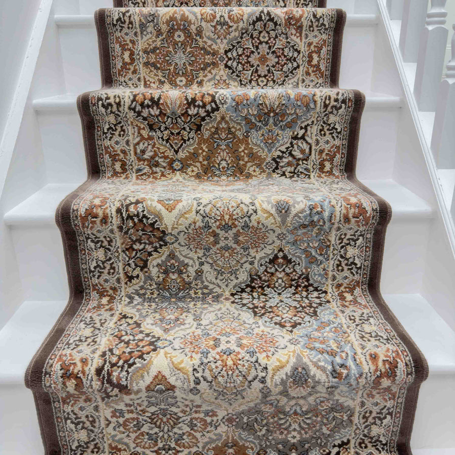 The Ancient Garden 57008-9696 Runner Rug, featuring intricate beige, brown, and blue floral patterns, is centered on a white-painted staircase for a traditional and elegant look.