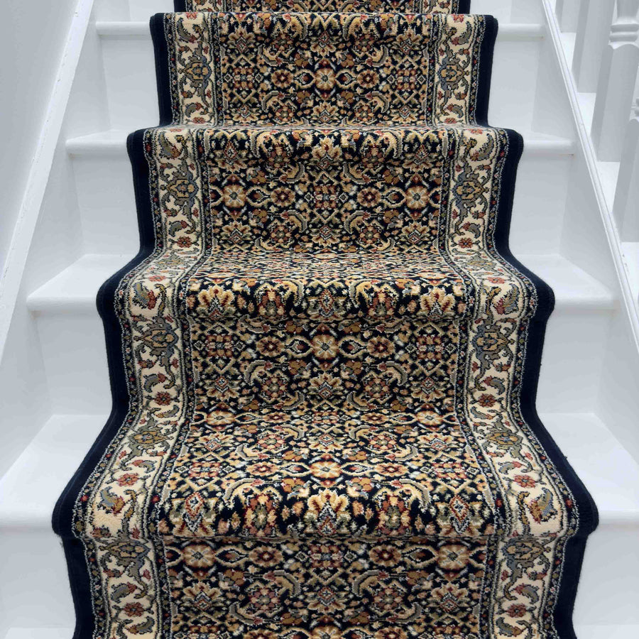 The Ancient Garden 57011-9666 Runner Rug, featuring an intricate floral pattern and dark borders in beige, red, and black, graces a white-painted staircase as a strikingly ornate hallway accent.