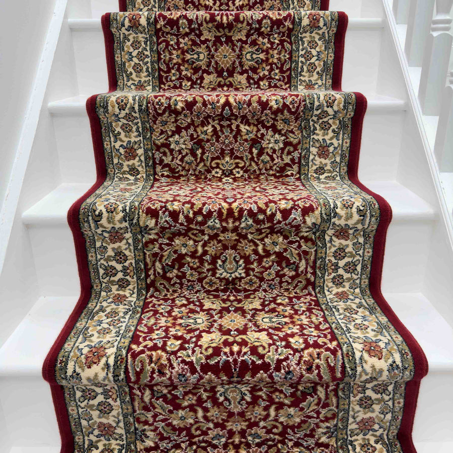 A white staircase features the Ancient Garden 57078-1414 Runner Rug, its red, beige, and blue floral and geometric patterns running down the center—ideal for hallways or entryways.