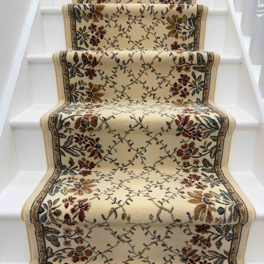 The Ancient Garden 57084-6464 Runner Rug, cream-colored with red, brown, and green floral and vine patterns, adds elegant charm to the center of white wooden stairs, perfect for enhancing your entryway like a classic hallway runner.