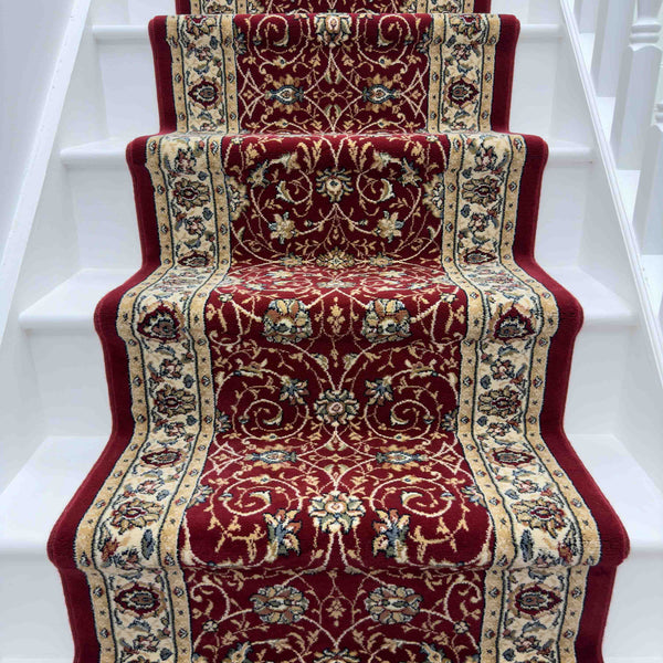 A white staircase features the Ancient Garden 57120-1464 Runner Rug, showcasing intricate red and beige floral and vine designs down the center, adding timeless elegance as a stunning hallway rug.