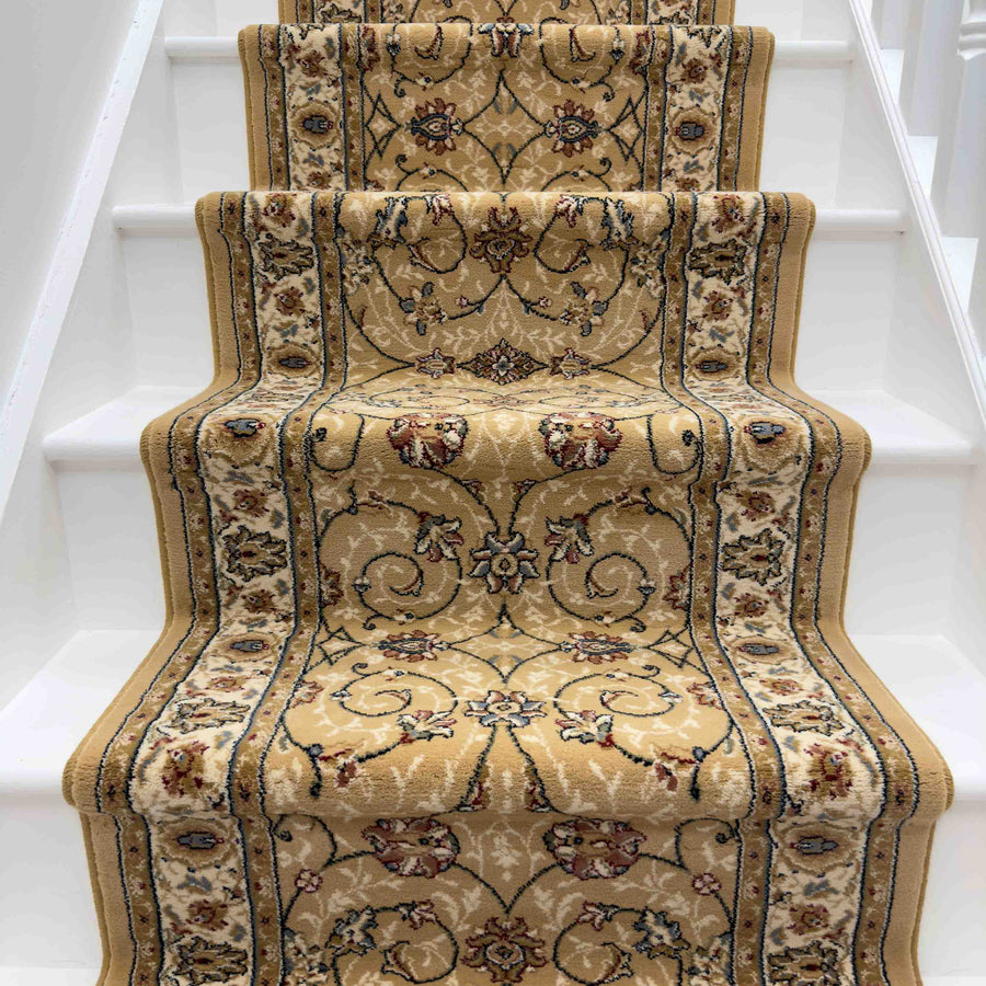 The Ancient Garden 57120-1464 Runner Rug, featuring beige and gold tones with floral and vine designs, covers white stairs for a traditional, elegant look—perfect as an entryway or hallway rug.