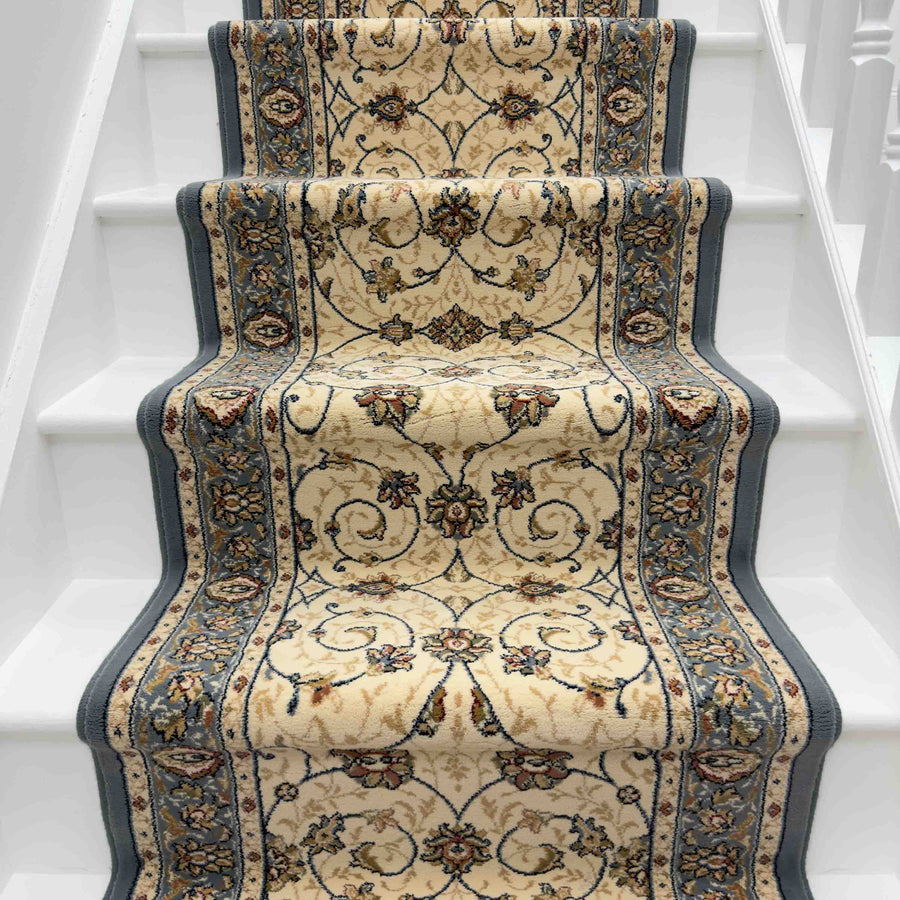 A white staircase with an Ancient Garden 57120-3464 Runner Rug in beige and blue, featuring floral and scroll designs, runs up the middle of the steps.