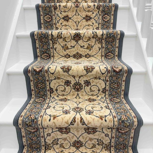 A white staircase with an Ancient Garden 57120-3464 Runner Rug in beige and blue, featuring floral and scroll designs, runs up the middle of the steps.