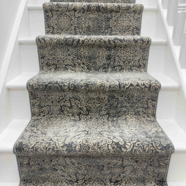 A staircase with white steps is adorned by the Ancient Garden 57162-3696 Runner Rug in gray and cream, showcasing intricate, ornate patterns for an elegant look.