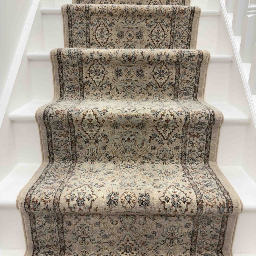 The Ancient Garden 57276-9295 Runner Rug, with its traditional floral design in beige and brown tones, covers the middle of a white-painted staircase and adds intricate elegance to your entryway.