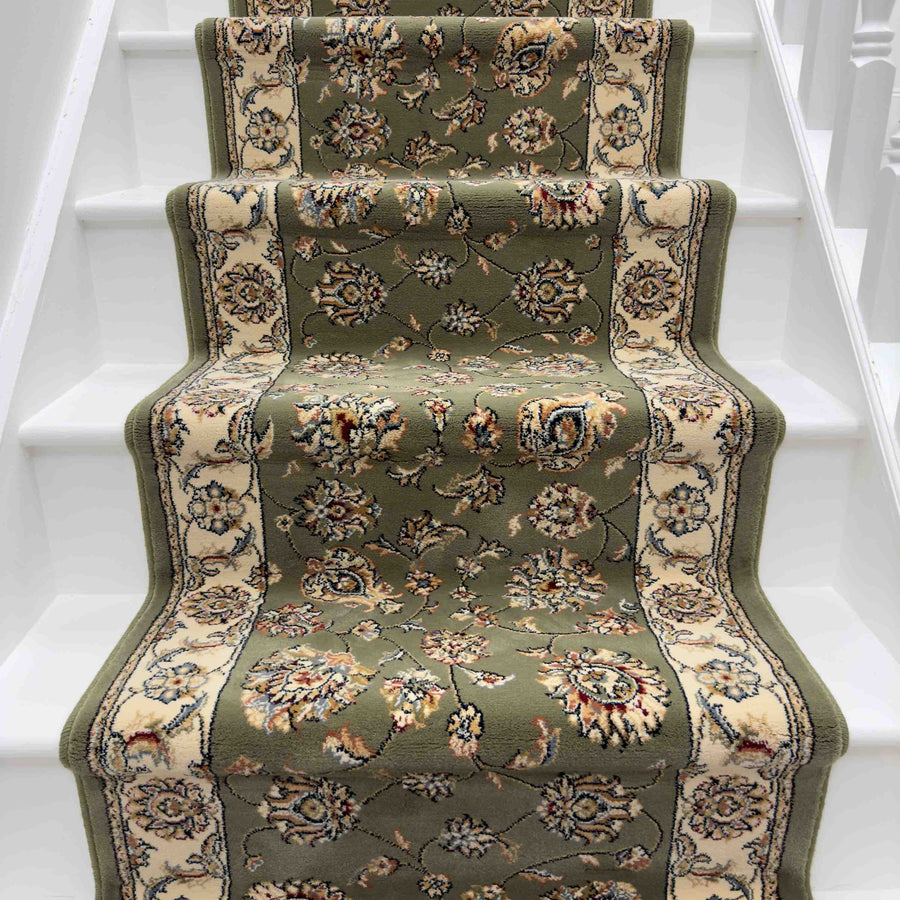 The Ancient Garden 57365-4464 Runner Rug, featuring green and beige floral patterns, is laid on white-painted stairs, covering the center steps and leaving the edges exposed for a classic, refined effect.