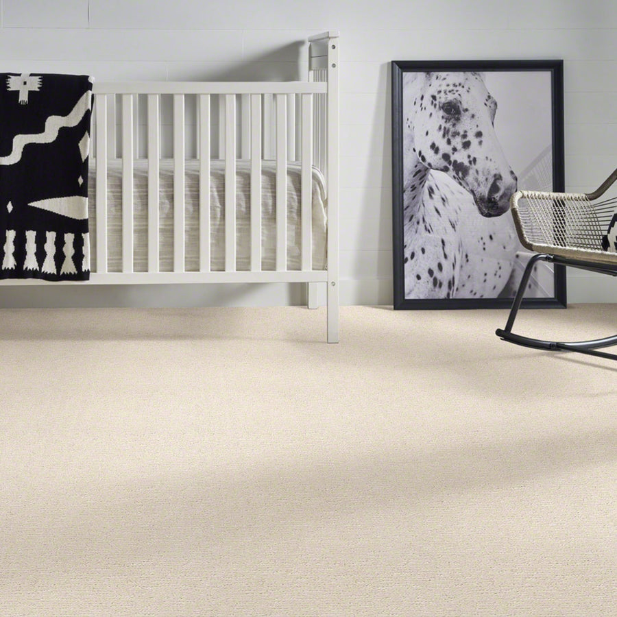 A white crib with a black and white blanket sits in a room with light carpet. Next to it, there is a framed photo of a spotted horse leaning against the wall and part of a black rocking chair is visible.