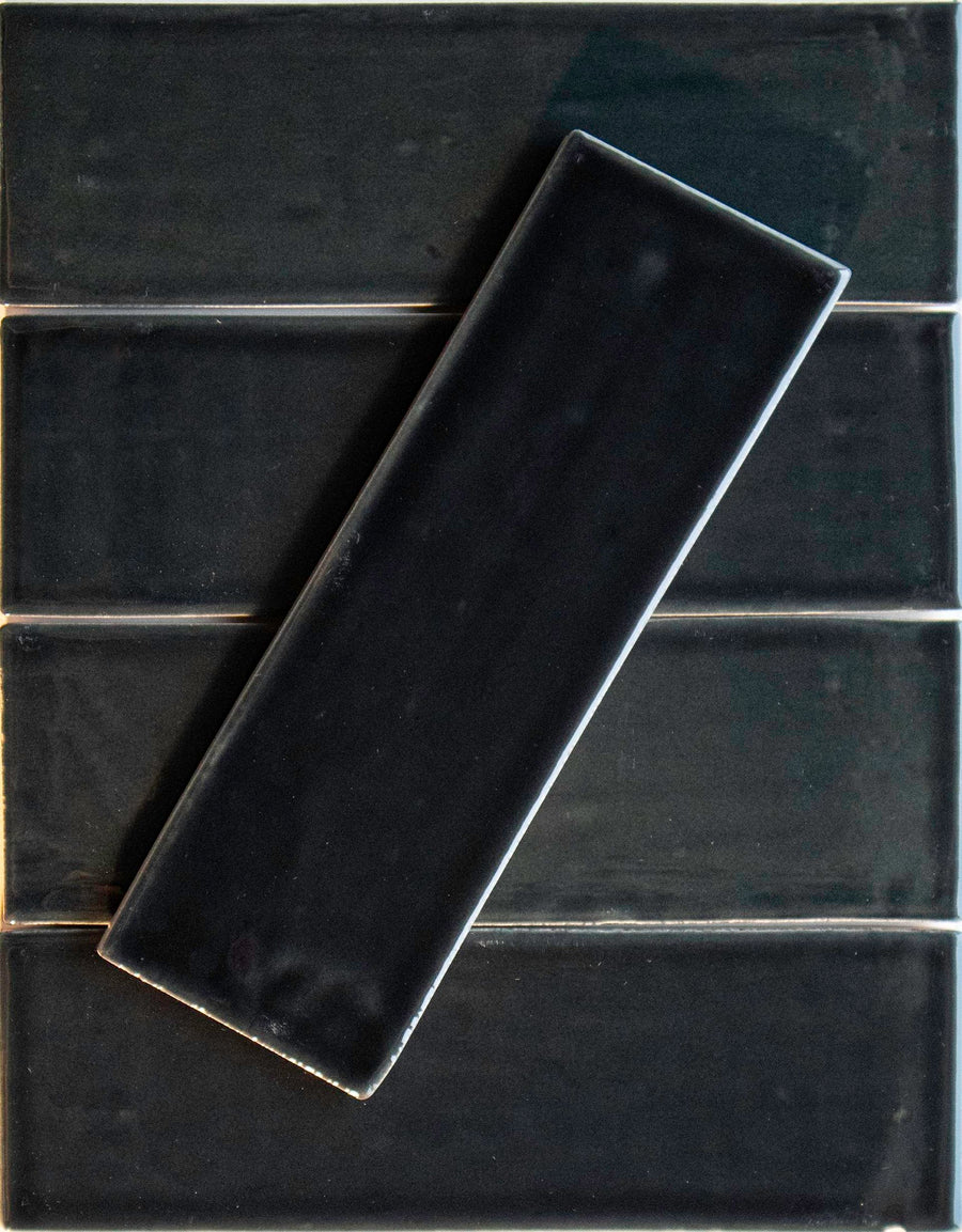 Five Noir Crackle 2.5x8 Ceramic Tiles in Aqua-holic are arranged horizontally, with one hand-dipped tile placed diagonally above. The tiles showcase a glossy, crackled surface and visible grout lines.