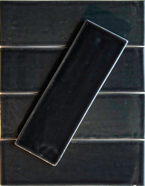 Five Noir Crackle 2.5x8 Ceramic Tiles in Aqua-holic are arranged horizontally, with one hand-dipped tile placed diagonally above. The tiles showcase a glossy, crackled surface and visible grout lines.