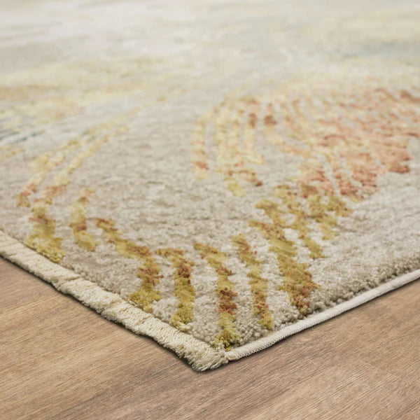 A close-up of a beige area rug with subtle yellow and orange patterns, placed on a light wood floor. The edge of the rug is visible, showing its plush texture and thickness.
