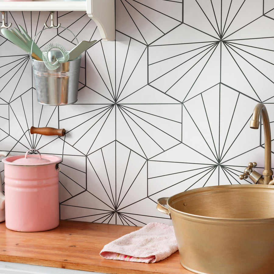 A kitchen counter with a gold sink, tan faucet, pink canister, metal utensil holder, and a pink towel. The backsplash features a geometric black-and-white starburst pattern.