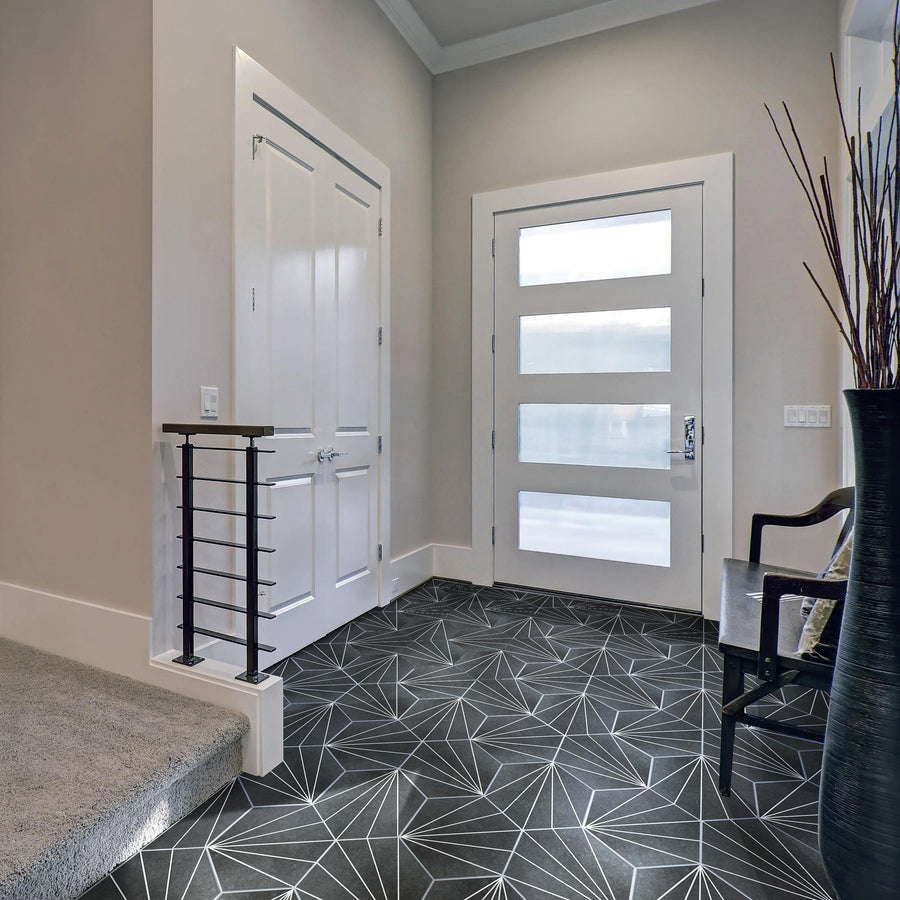 Modern entryway with geometric black and white tile flooring, a white door with horizontal glass panels, neutral walls, and a staircase with carpet and metal railing on the left. A black vase and chair are on the right side.