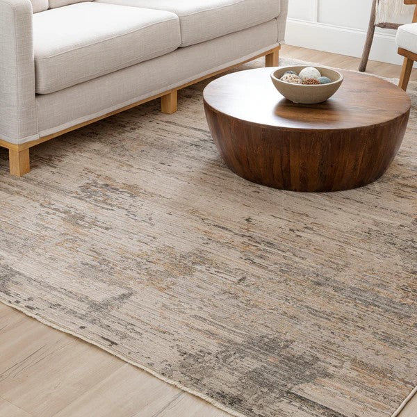 A modern living room with a light beige sofa, a round wooden coffee table with decorative bowls, and a textured, neutral-toned area rug on a light wood floor.