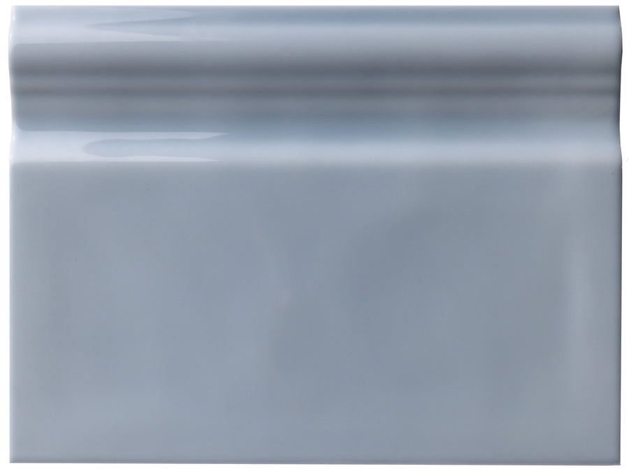 The Zephyr 6x8 Ceramic Baseboard is a rectangular, glossy light gray tile with a raised, rounded top edge, inspired by handcrafted luxury and ideal for Mediterranean-style baseboards.
