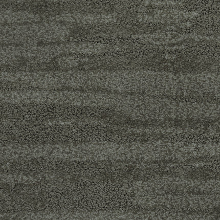 A close-up of the Cirrus Berber Carpet in Basil shows a textured surface with mottled, uneven patterns and subtle shading variations, resembling premium flooring with a rough, granular look.