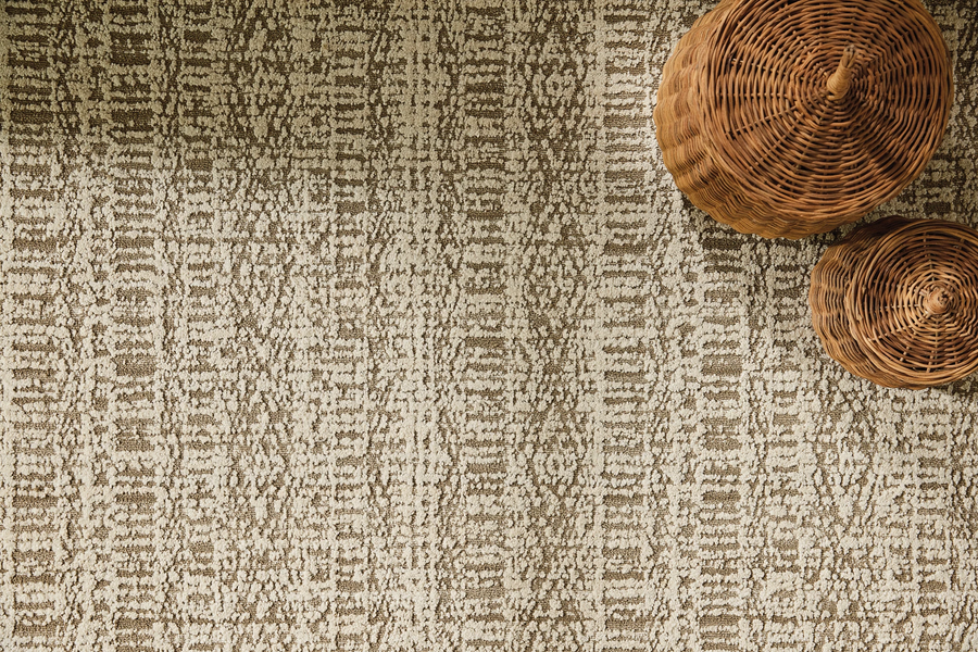 Two round, woven wicker baskets are placed on a beige and brown textured patterned rug, viewed from above. Shadows fall across part of the rug and baskets.