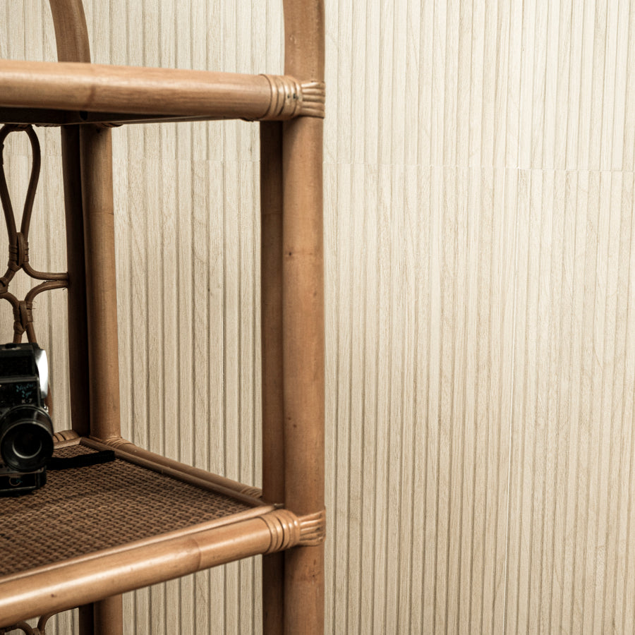 A vintage camera sits on the lower shelf of a bamboo shelving unit against a textured beige wall.