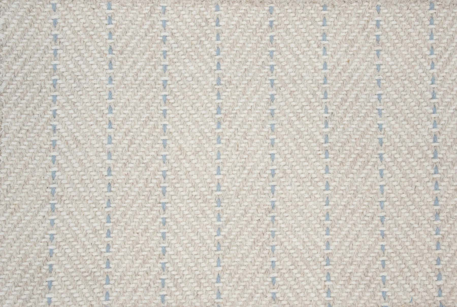 Close-up of Angola Berber Carpet in Beach color, featuring a cream base with blue vertical dashed lines in a herringbone pattern, evoking Angola flooring. The soft, slightly raised texture adds contemporary appeal.