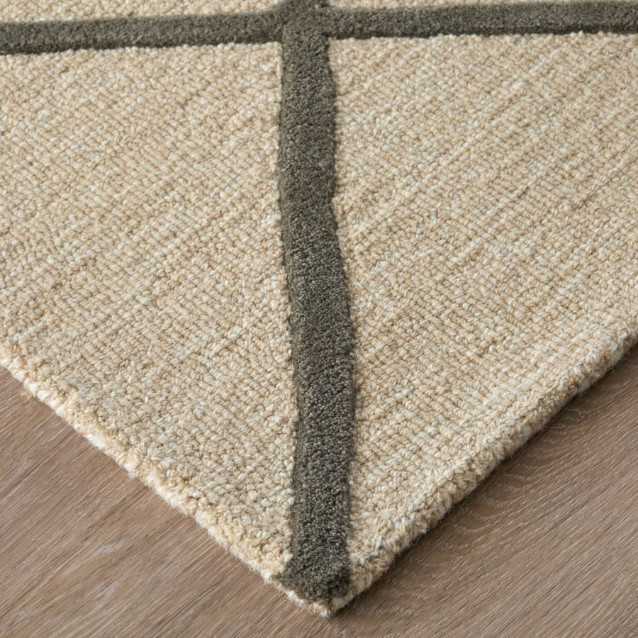Close-up of the corner of a beige textured rug with thick dark brown lines forming a cross pattern, placed on a light wood floor.