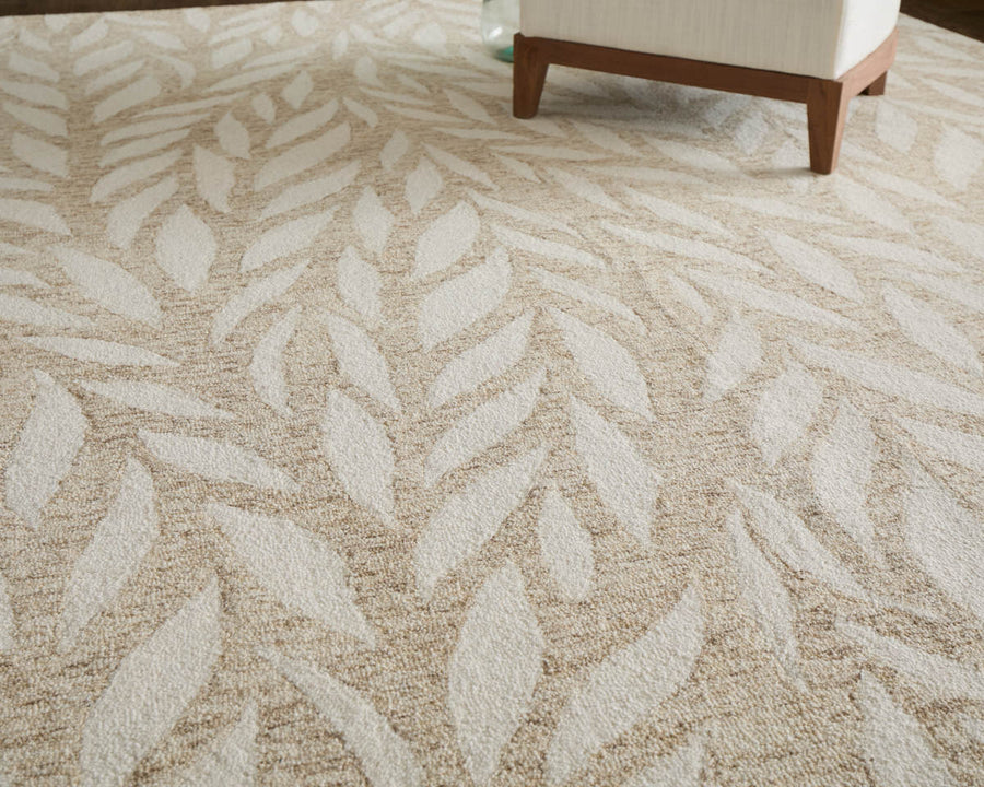 Beige and cream area rug with a subtle leaf pattern, shown partially under the leg of a white upholstered chair.