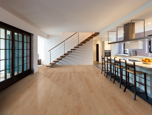 Modern open-plan kitchen and dining area with light wood floors, a large island with bar stools, sleek staircase with glass railing, and French doors on the left letting in natural light.