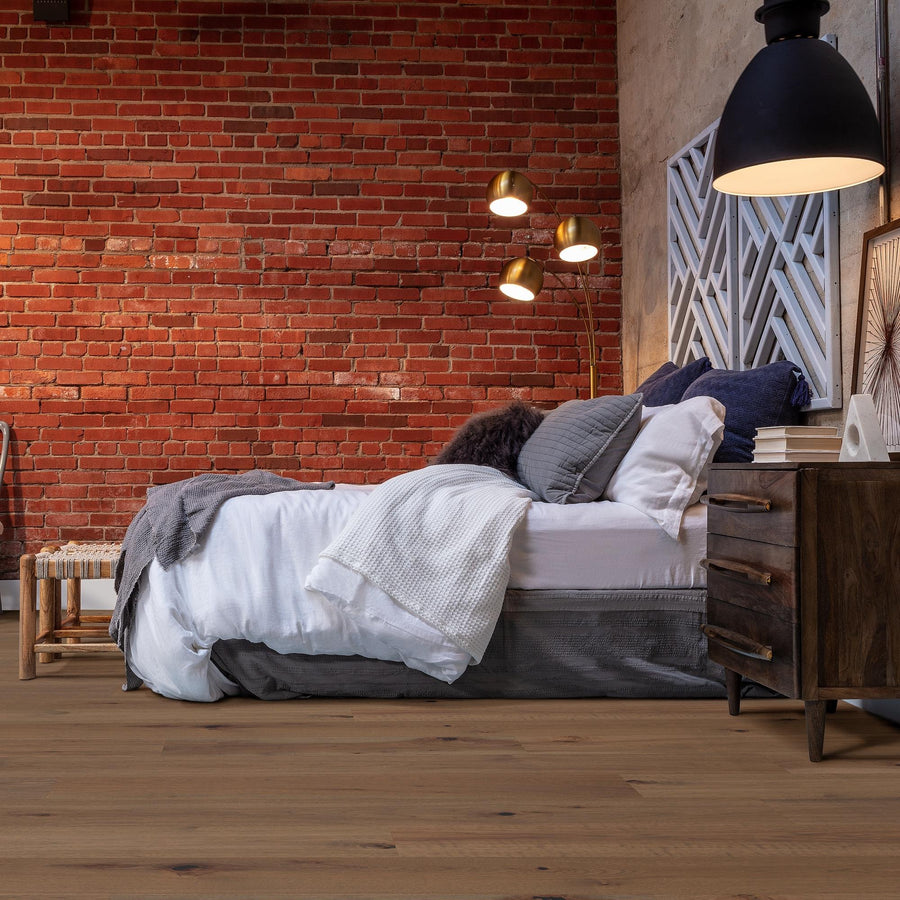 A cozy bedroom with a red brick wall, modern wood furniture, a neatly made bed with white and gray bedding, decorative pillows, and a black pendant light above a nightstand.